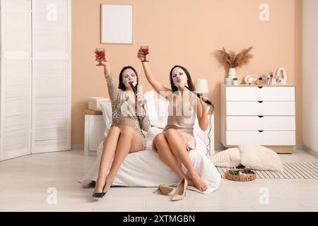 Beautiful young women with facial masks, curling irons and wine singing in bedroom Stock Photo