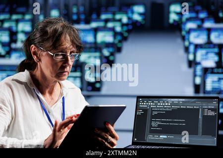 Old computer scientist writing script code in data center on laptop terminal. Adept professional doing maintenance work in server room, updating rigs software to prevent malfunctions Stock Photo