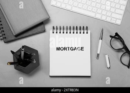 Word Mortgage in notebook, eyeglasses and computer keyboard on grey table, flat lay Stock Photo