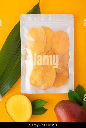 Large pack of dried mango slices with leaf and raw mango on yellow background.Macro Stock Photo
