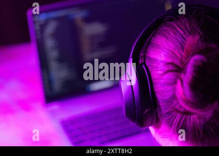 woman software developer in modern wireless headphones against laptop screen with software code, neon light, for software development ,education topic Stock Photo
