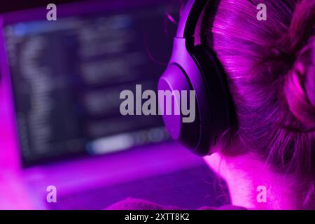 woman software developer in modern wireless headphones against laptop screen with software code, neon light, for software development ,education topic Stock Photo