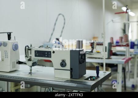 Row of desks with electric sewing machines and other tailoring equipment standing in spacious modern atelier or workshop Stock Photo