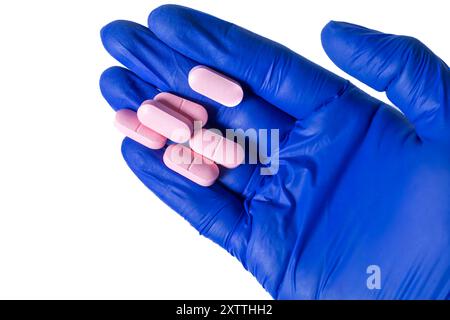 Blue gloved hand holds pink pills on white background. Top view Stock Photo