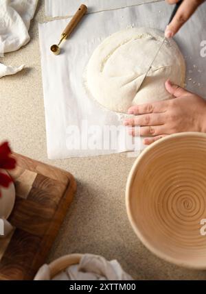 Hands cutting dough with a knife on parchment paper, next to a p Stock Photo