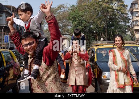 Guests at an Indian wedding celebration spill out in the street to dance, a man carrying his son on his shoulders while dancing; Mumbai, India Stock Photo