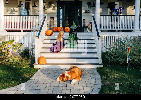 Children in costumes sit on porch steps with pumpkins and dog Stock Photo