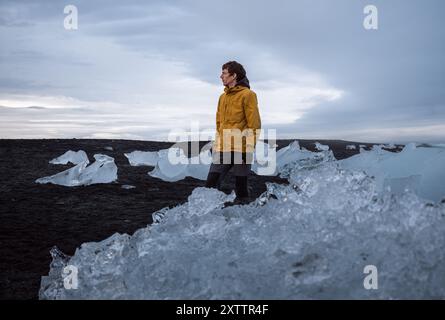 young man in yellow jacket stands at the Diamond Beach, Iceland Stock Photo