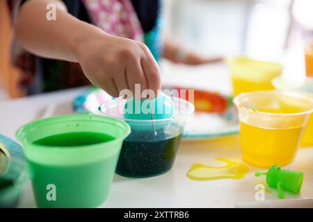 Child's hand dipping an Easter egg in colorful dye cups Stock Photo