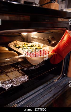 Person removing roasted vegetables on a tray from oven Stock Photo