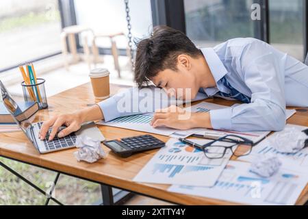 Tired and overworked young businessman falling to sleep while working late in his office Stock Photo