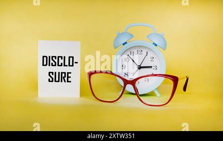 The word DISCLOSURE is written in a notepad. Clock and glasses on a yellow background Stock Photo
