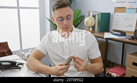 Young hispanic man counting mexican pesos in an office setting, looking focused and professional. Stock Photo