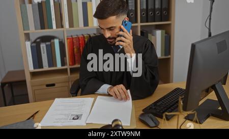 Handome man with beard wearing judge's robe, in office, talking on phone and looking at paperwork Stock Photo