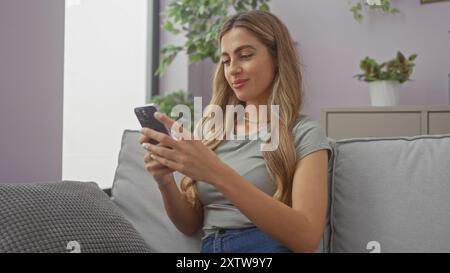 A young woman engages with her smartphone on a couch, conveying leisure in a cozy living room setting. Stock Photo