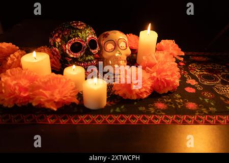 View from above of a skull embellished with metallic flowers, surrounded by vivid orange marigolds and lit candles. The black backdrop and Day of the Stock Photo