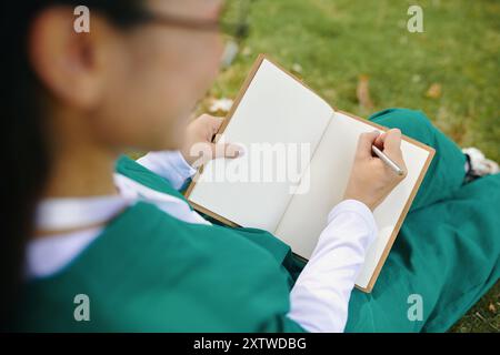 Person Writing in Notebook on Lawn in Green Attire Stock Photo