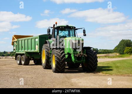 Green John Deere 6195m utility tractor with tipping grain trailer. Stock Photo