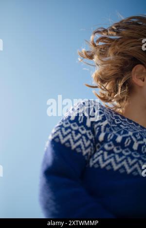 Close-up of a person with curly hair wearing a blue and white patterned sweater against a clear sky. Stock Photo