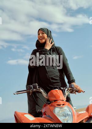 Smiling woman in a hijab riding a red scooter under a clear blue sky. Stock Photo