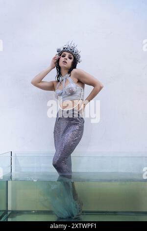 A young woman in a mermaid costume stands in a glass tank filled with water, her tail shimmering. Stock Photo