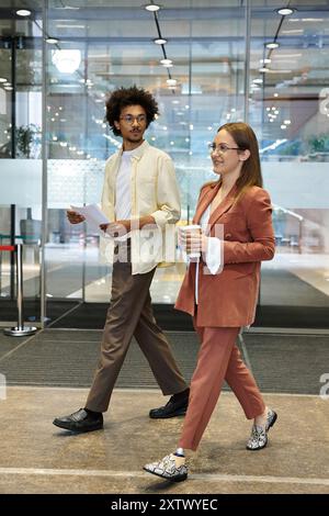 Two colleagues, one with a prosthetic leg, chat and walk through an office lobby. Stock Photo