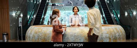 Three colleagues chat in an office lobby, with an escalator in the background, showcasing diversity. Stock Photo