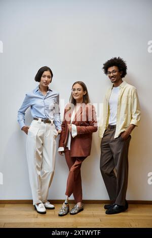 Three colleagues stand together in a modern office, chatting and laughing. Stock Photo