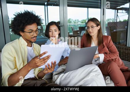 Three colleagues, diverse in race, collaborate on a project while enjoying the view from a modern office rooftop. Stock Photo