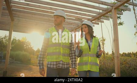 Two successful Caucasian workers man male guy female woman girl builders walking stroll under construction structure planning discuss unfinished Stock Photo