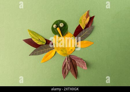 Creative craft project on green background. Bird crafted from leaves, yellow leaf body, colorful leaf wings and tail. top view Stock Photo