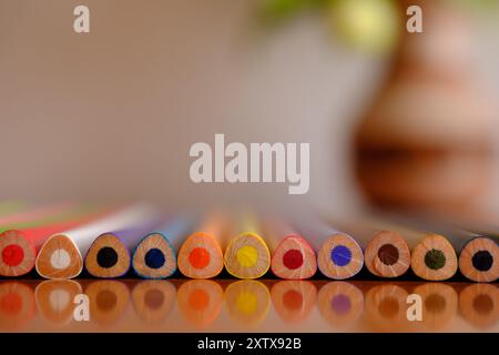 Background of colored pencils with a triangular shape in close focus and reflected on a shiny wooden surface. Stock Photo