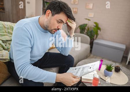 Worried man sitting on couch looking at bills Stock Photo