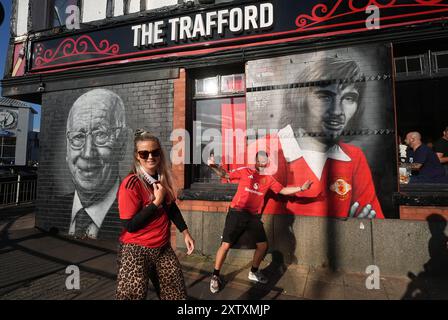 Manchester United fans with a mural of former players Bobby Charlton and George Best near the ground ahead of the Premier League match at Old Trafford, Manchester. Picture date: Friday August 16, 2024. Stock Photo