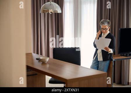 Caucasian senior woman reading documents while talking on the mobile phone in hotel Stock Photo