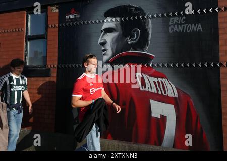 Manchester United fans with a mural of former player Eric Cantona near the ground ahead of the Premier League match at Old Trafford, Manchester. Picture date: Friday August 16, 2024. Stock Photo