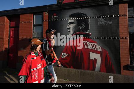 Manchester United fans with a mural of former player Eric Cantona near the ground ahead of the Premier League match at Old Trafford, Manchester. Picture date: Friday August 16, 2024. Stock Photo