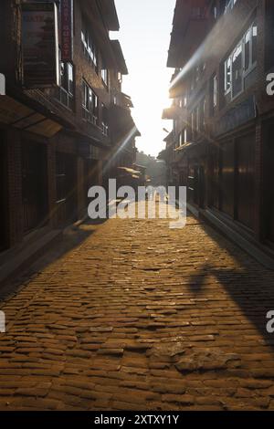 Bhaktapur, Nepal, October 31, 2013: Sun rays shoot down brick cobblestone road among alleys around historic Bhaktapur Durbar Square at morning time. B Stock Photo