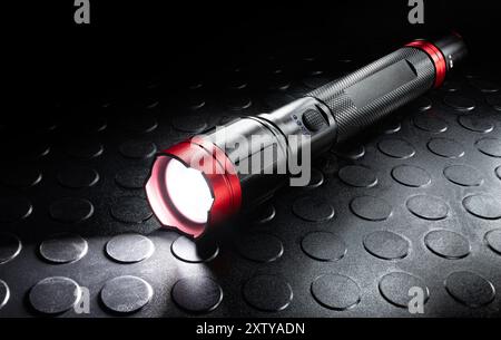 Rechargeable black and red metal flashlight with its LED activiated that is ideal for power outages, hurricanes of other natural disasters. Stock Photo
