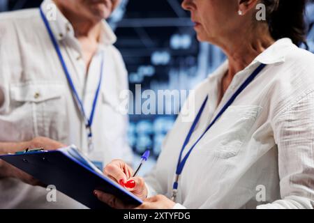 Elderly engineers performing diagnostic assessments on server rigs to detect problems with data center hardware. Repairmen diligently reviewing maintenance list examining for potential system errors Stock Photo