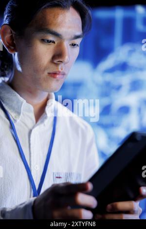 Computer scientist using tablet in data center to maintenance artificial intelligence neural networks simulating human thought processes in computerized model. Asian man doing checkup on AI systems Stock Photo