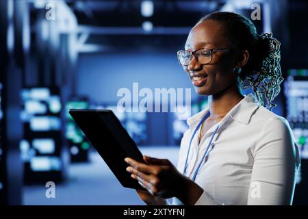 Smiling woman between server hub rows providing processing resources for businesses worldwide. Happy admin fixing data center mainframes tasked with managing massive databases Stock Photo