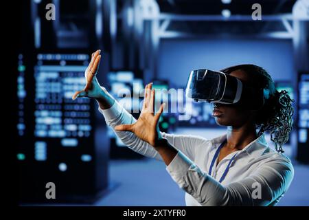 Tech support in data center uses virtual reality to prevent system overload. BIPOC VR technology user in server room ensuring enough network bandwidth for smooth operations Stock Photo