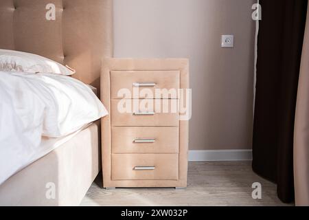 Beige dresser with four drawers near the bed. Well organized bedroom in natural light. Stock Photo