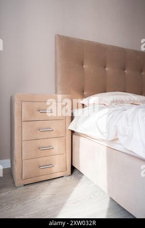 Beige dresser with four drawers near the bed. Well organized bedroom in natural light. Stock Photo