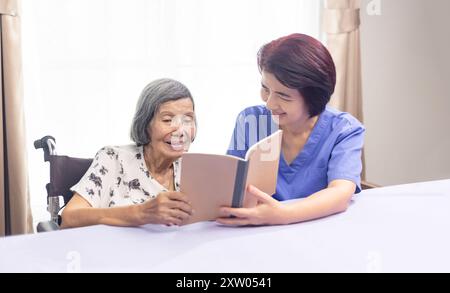Elderly woman reading aloud a book for dementia therapy with caregiver. Stock Photo