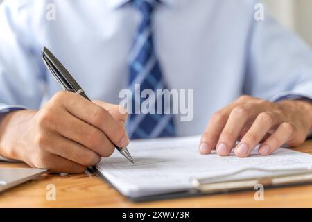 Close up of hands of a businessman holding a pen while writing on a document Stock Photo