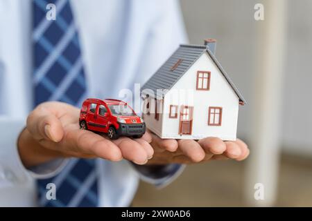 Close up hands of a male realtor holding a house and car model in his hands, home buying or real estate concept Stock Photo