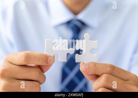 Close up hands of a businessman holding 2 jigsaw puzzle piecess trying to put them together Stock Photo