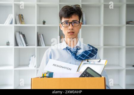 Sad young businessman holding a box full of his office stuff while walking out of his office after resigned from work Stock Photo